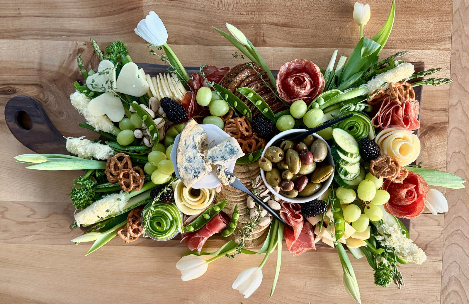 A live edge curved handle walnut charcuterie beautifully dressed with a spring theme that pops. Added tulips for a spring feel.