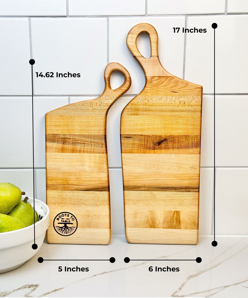 Two handcrafted wooden boards made from edge grain maple. Both feature ergonomic handles with a soft, rounded design, displayed on a textured fabric backdrop for a rustic aesthetic.