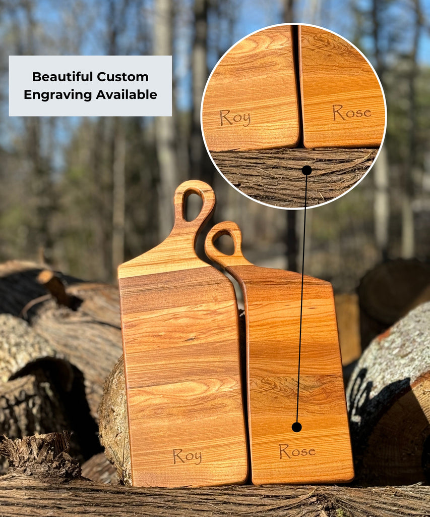 Two handcrafted wooden boards made from edge grain maple. Both feature ergonomic handles with a soft, rounded design, displayed on a textured fabric backdrop for a rustic aesthetic. Engraving is highlighted