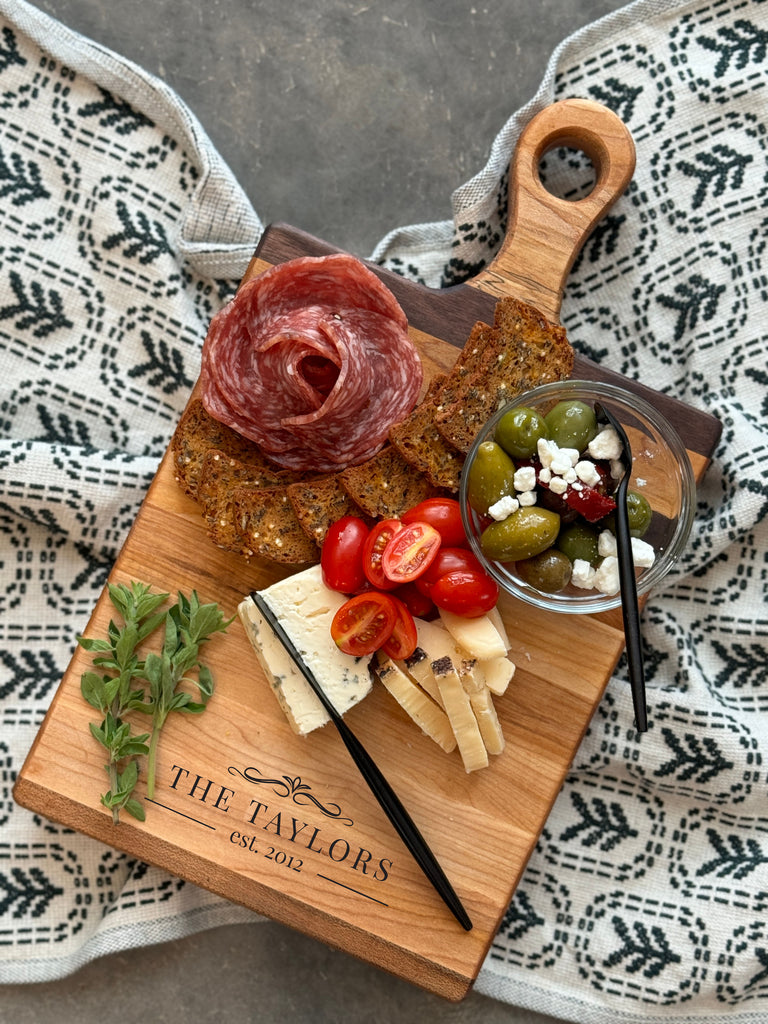 Small personalized wooden charcuterie / cutting board with The Taylors est. 2012 engraving. Featuring elegant walnut and maple edge grain stripes. Perfect for hosting and gifting.