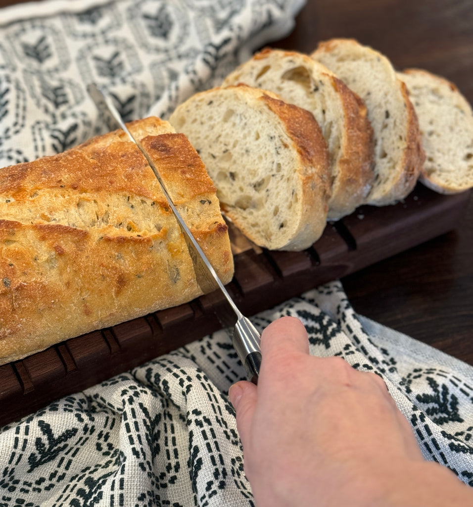 A hand shown slicing bread on a solid walnut board.