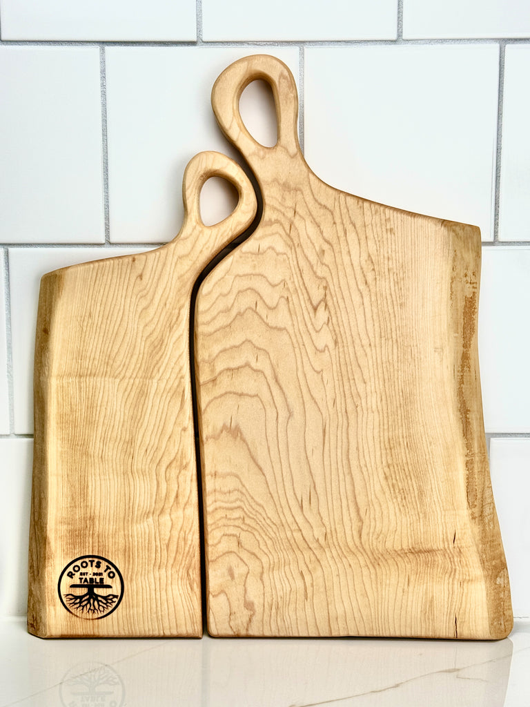 A pair of handcrafted wooden live edge boards engraved with Charlene & Jason, designed to nestle together. The handles fit snugly, symbolizing the intimate connection of a woman resting her head on a man's shoulder, creating one harmonious piece.