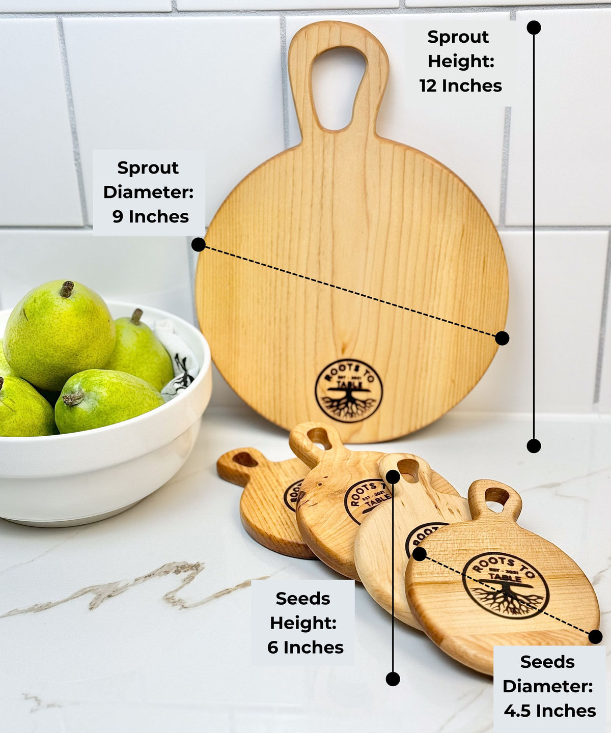 Round wooden cutting boards from Roots to Table, labeled with dimensions: Sprout board (12 inches tall, 9-inch diameter) and Seeds boards (6 inches tall, 4.5-inch diameter). Displayed on a white counter with pears in a bowl nearby.