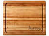 An extra large rectangular wooden cutting board with a raised rim and channeled edges for a juice groove, featuring a natural maple honey-toned wood grain and an engraved script logo reading The Maple Family Est. 2024 in the bottom right corner.