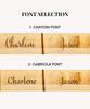 Font selection options displayed on wooden surfaces:
1. Cantoni Font - Elegant, classic style with clean lines.
2. Gabriola Font - Flowing, cursive design with a more artistic flair.