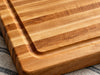 A close-up of an edge grain wooden cutting board with a raised rim and juice groove.