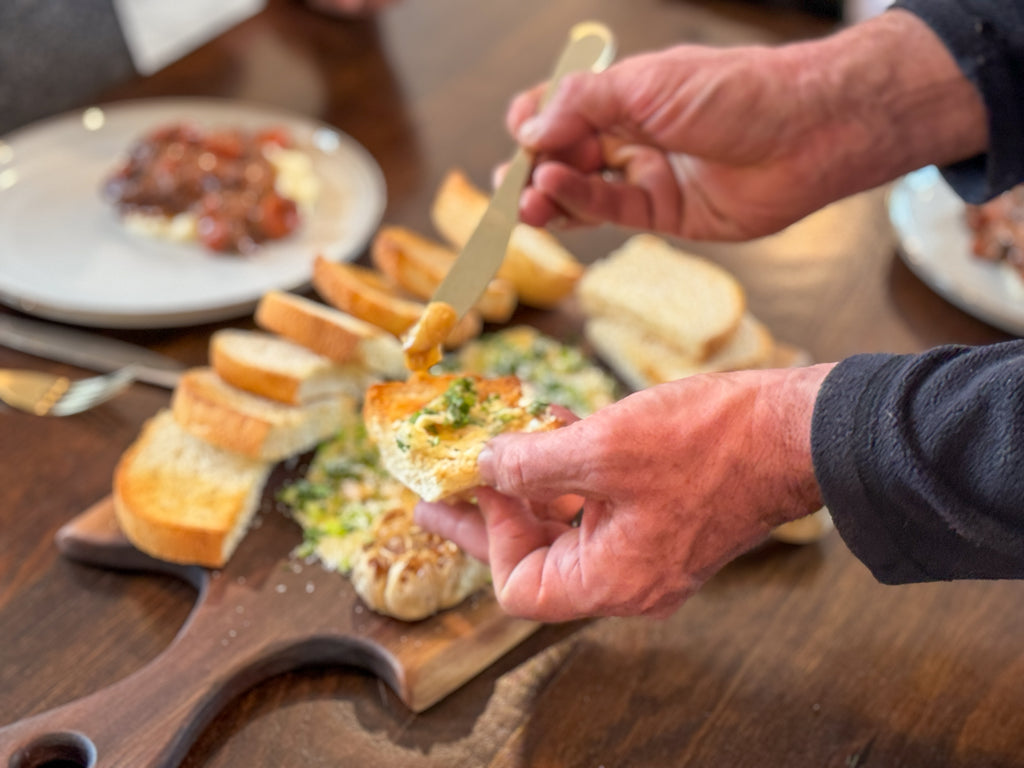 A man spreads butter onto bread above a walnut live edge charcuterie board