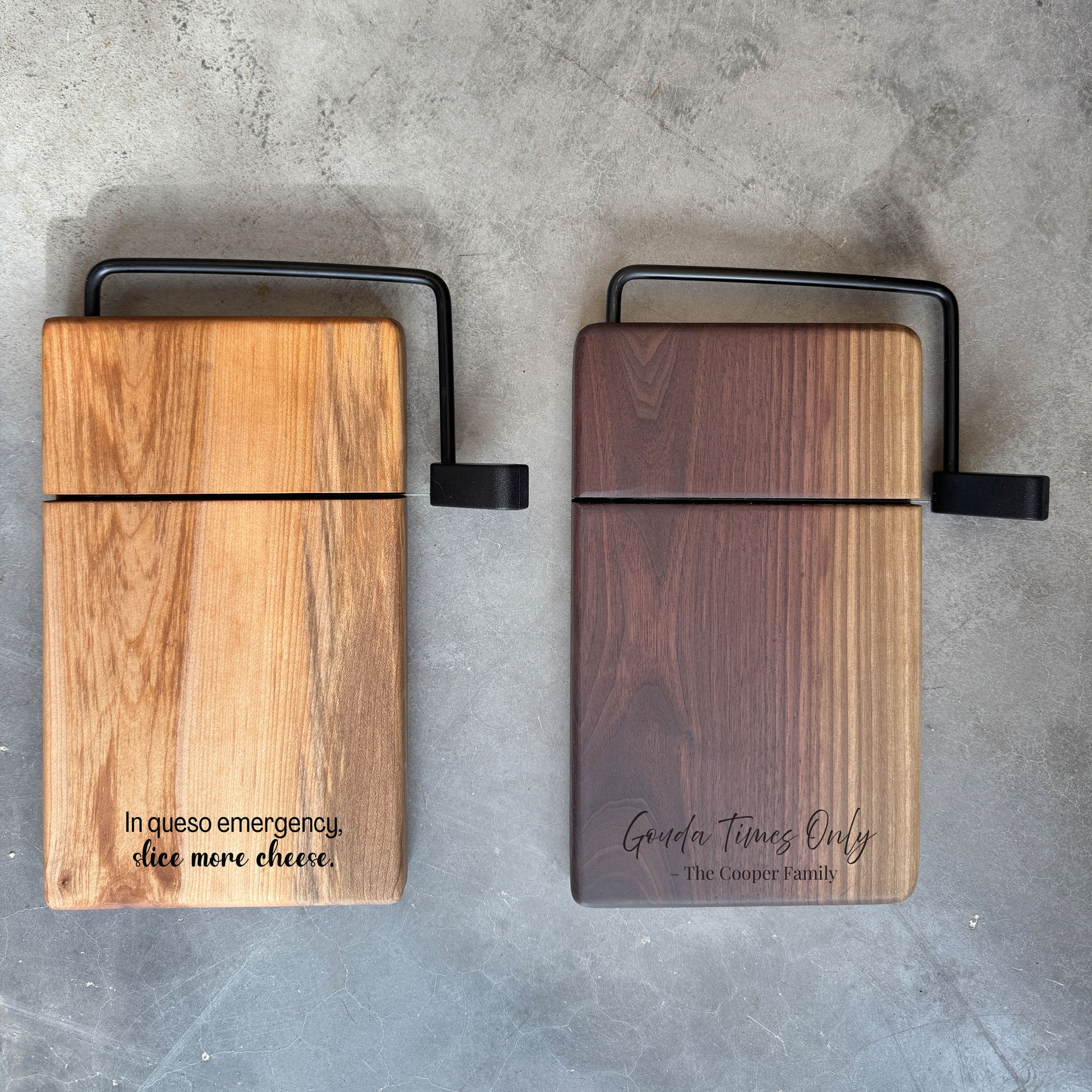2 cheese slicer cutting boards on a countertop side by side. One cheese slicer has a wlanut base, and the other has a maple wood base. both cheese wire slicer boards are engraved with a fun quote. The board measures 5.75 x 9.5 x 1 inch thick, with wire slicer attachment. Custom Engraving available