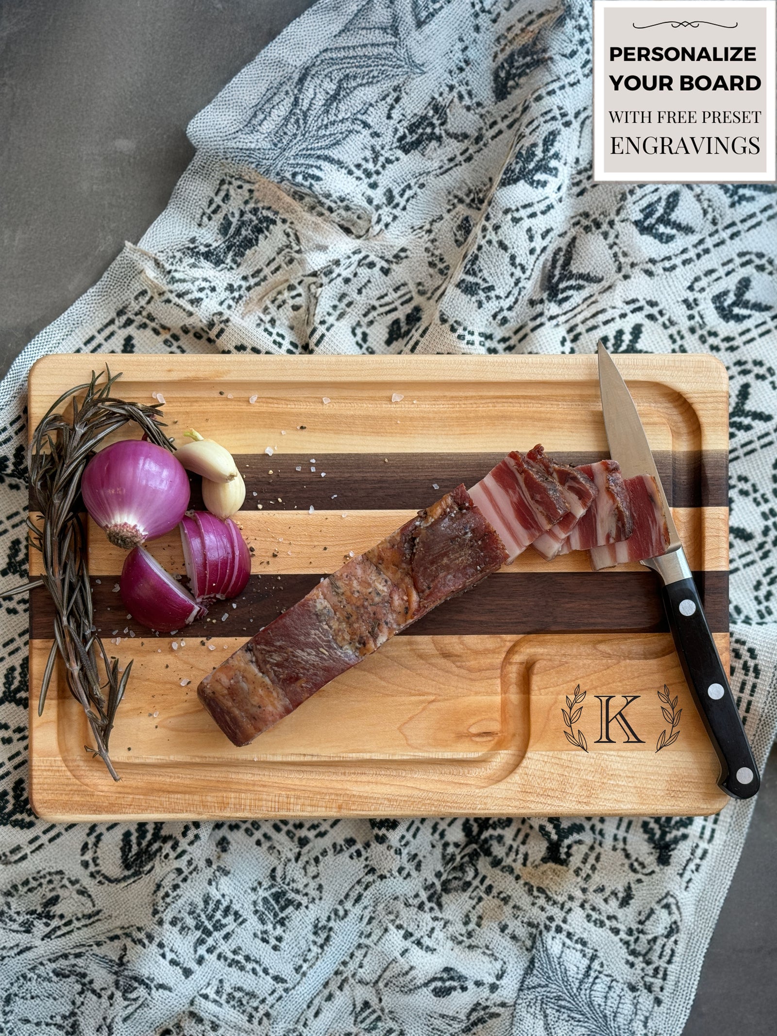 A handcrafted cutting board made from alternating strips of maple and walnut wood, featuring a juice groove for functionality and a smooth, polished finish. A customized letter W engraving surrounded by laurel leaves in the corner.