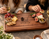 Two friends enjoying wine, cheese, crackers and fresh fruit served on a custom personalized walnut charcuterie board. The board features an engraved illustration of two friends and a meaningful friendship quote. Handcrafted hardwood serving board with juice groove and subtle rubber feet, perfect for entertaining or gifting to a best friend.