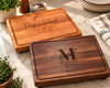 Two handcrafted personalized wooden cutting boards displayed together, showcasing different hardwood colours and custom engraving styles. Each board features beautiful natural wood grain, a routed juice groove and smooth rounded edges. Personalized cutting boards make thoughtful wedding, anniversary, housewarming and family gifts.