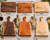 A collage showing three wooden serving boards in different wood tones: walnut, cherry, and maple. Each board has engraved personalized text and small decorative illustrations, with food and drink props around them.