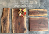 Four unique live-edge walnut charcuterie boards displayed on a rustic concrete surface. One board is adorned with crackers, olives, salami roses, and cheese. Engravings and natural wood grains highlight the individuality of each piece.