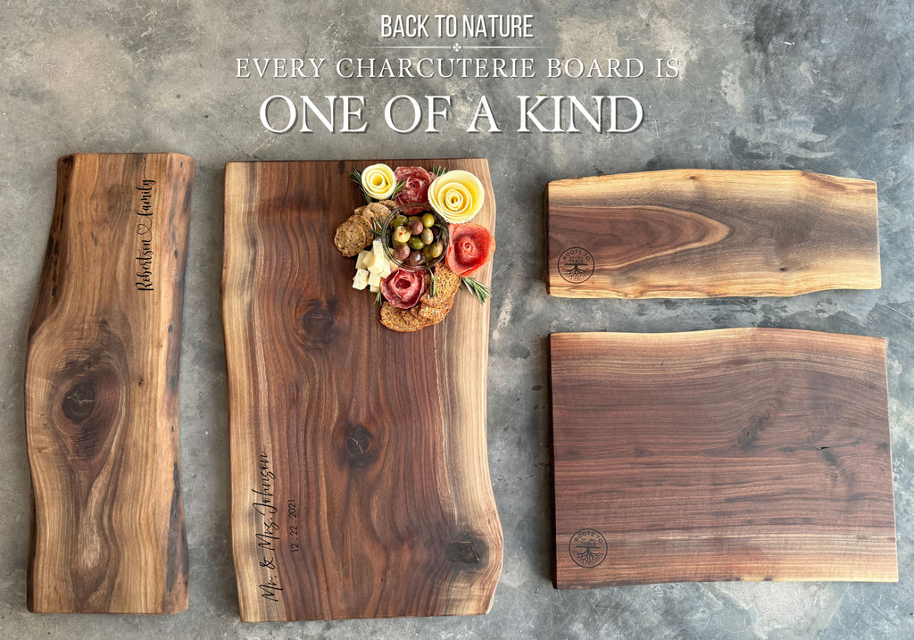 Four unique live-edge walnut charcuterie boards displayed on a rustic concrete surface. One board is adorned with crackers, olives, salami roses, and cheese. Engravings and natural wood grains highlight the individuality of each piece.