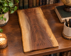 A rectangular walnut crib board with a live edge, engraved with the words 'The Godfreys Est 2005 displayed on a wooden table surrounded by books, a plant, and a candle.