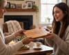 A wooden engraved serving board with handwritten recipe is gifted from grandmother to grand daughter in a touching moment.