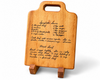 Maple cutting board with handwritten family recipe engraved onto the board. The board rests in a two piece wood stand.