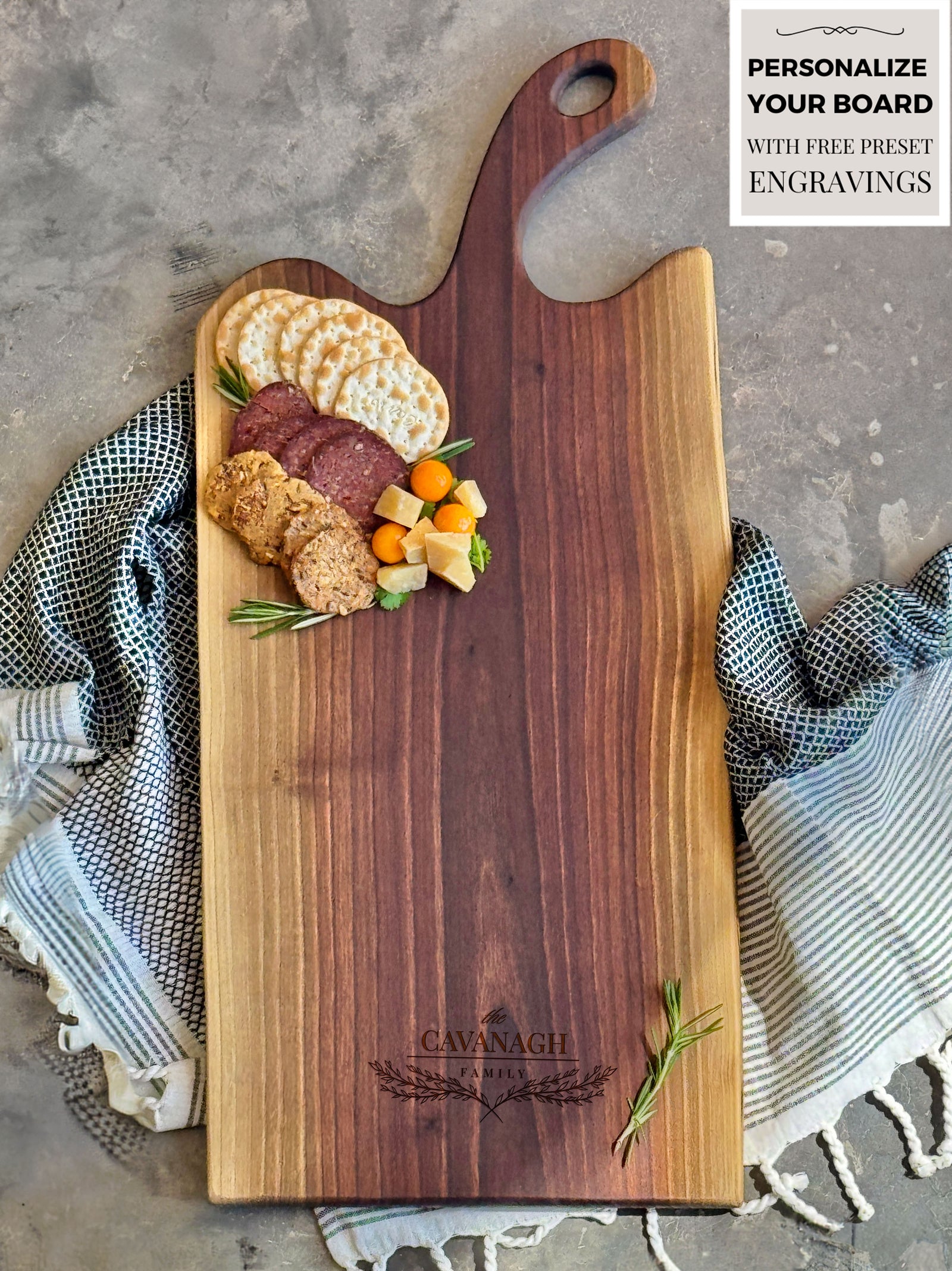 An extra-large personalized walnut heartwood charcuterie board featuring a rich pattern, engraved with The Cavanagh Family Topped with crackers, salami, cheese, and herbs, it rests on a textured cloth, showcasing rustic elegance and functionality.