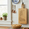 A personalized cutting board hangs on a kitchen wall as home decor, a hand written recipe is engraved on the maple wood.