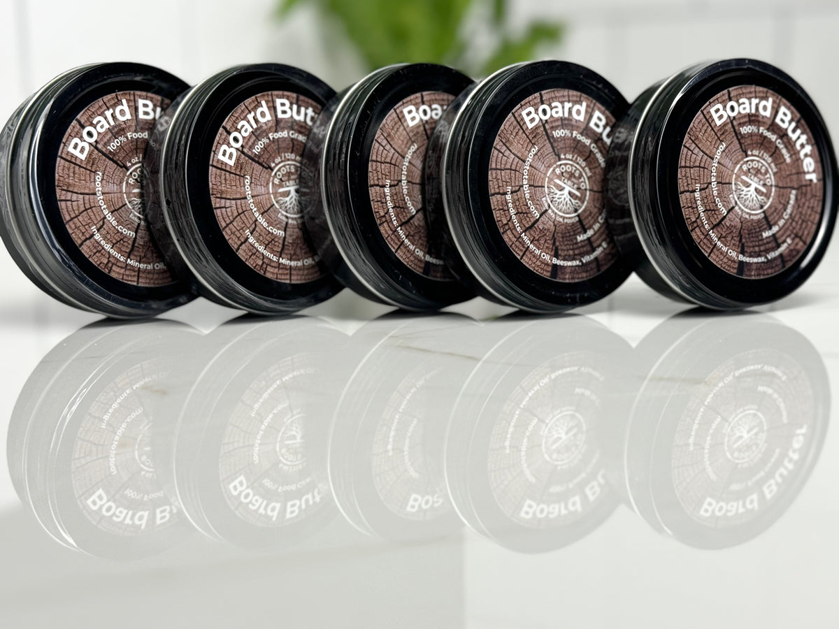 5 Tins of Roots to Table Board Butter, labeled as 100% food grade with ingredients including mineral oil, beeswax, and vitamin E. The product is displayed on a wooden surface with a "Pack of 4" label highlighted. Made in Canada, 4 oz/120 ml size.
