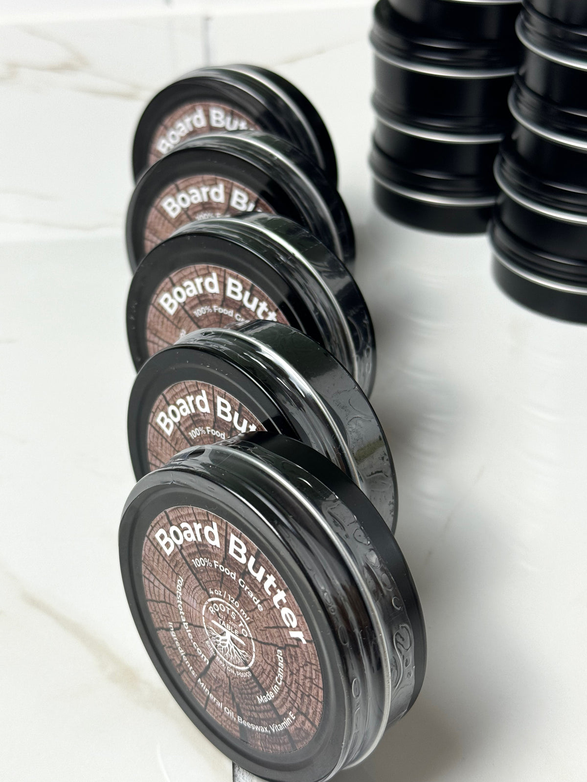 Tins of Roots to Table Board Butter, labeled as 100% food grade with ingredients including mineral oil, beeswax, and vitamin E. T