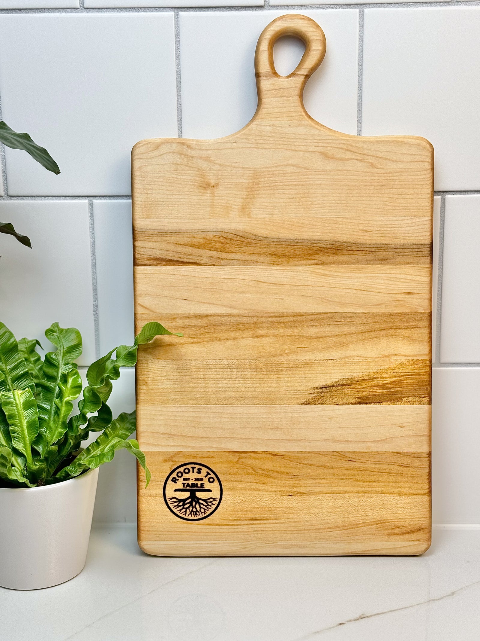 A personalized maple wood charcuterie board with The Williams Family engraving, beautifully arranged with cheese set on a concrete countertop.