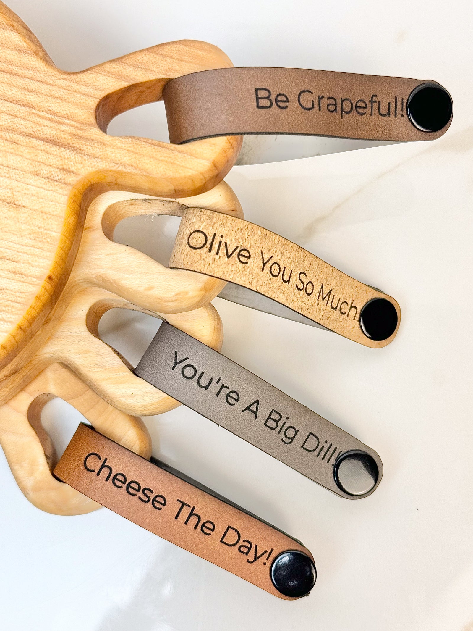 Maple wooden coaster single serve mini charcuterie board set with vegan leather straps engraved with puns: Be Grapeful!!, Olive You So Much, You're A Big Dill!, and Cheese The Day! Coasters have a natural finish.