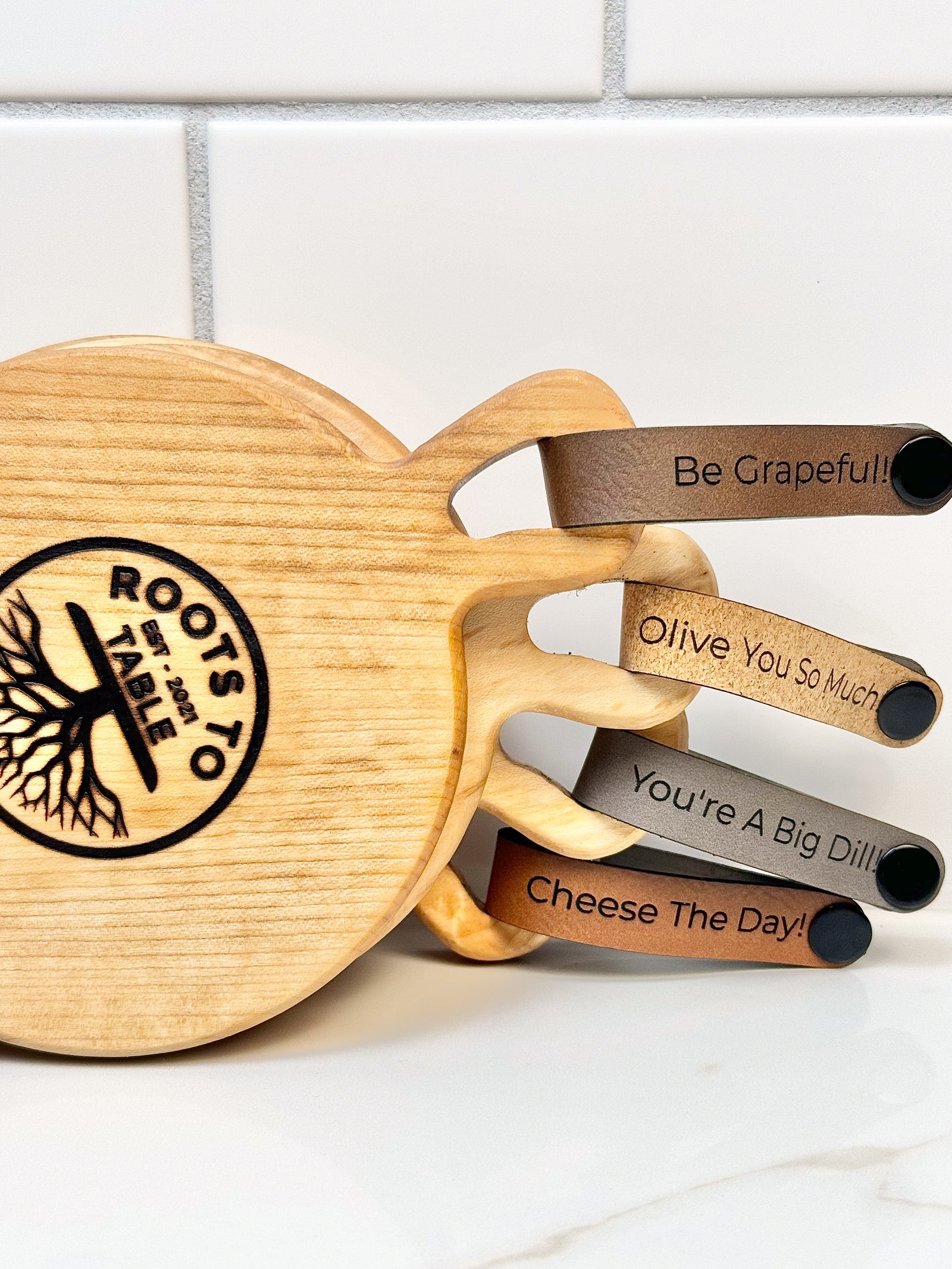 Maple wooden coaster single serve mini charcuterie board set with vegan leather straps engraved with puns: Be Grapeful!!, Olive You So Much, You;re A Big Dill!, and Cheese The Day! Coasters have a natural finish.