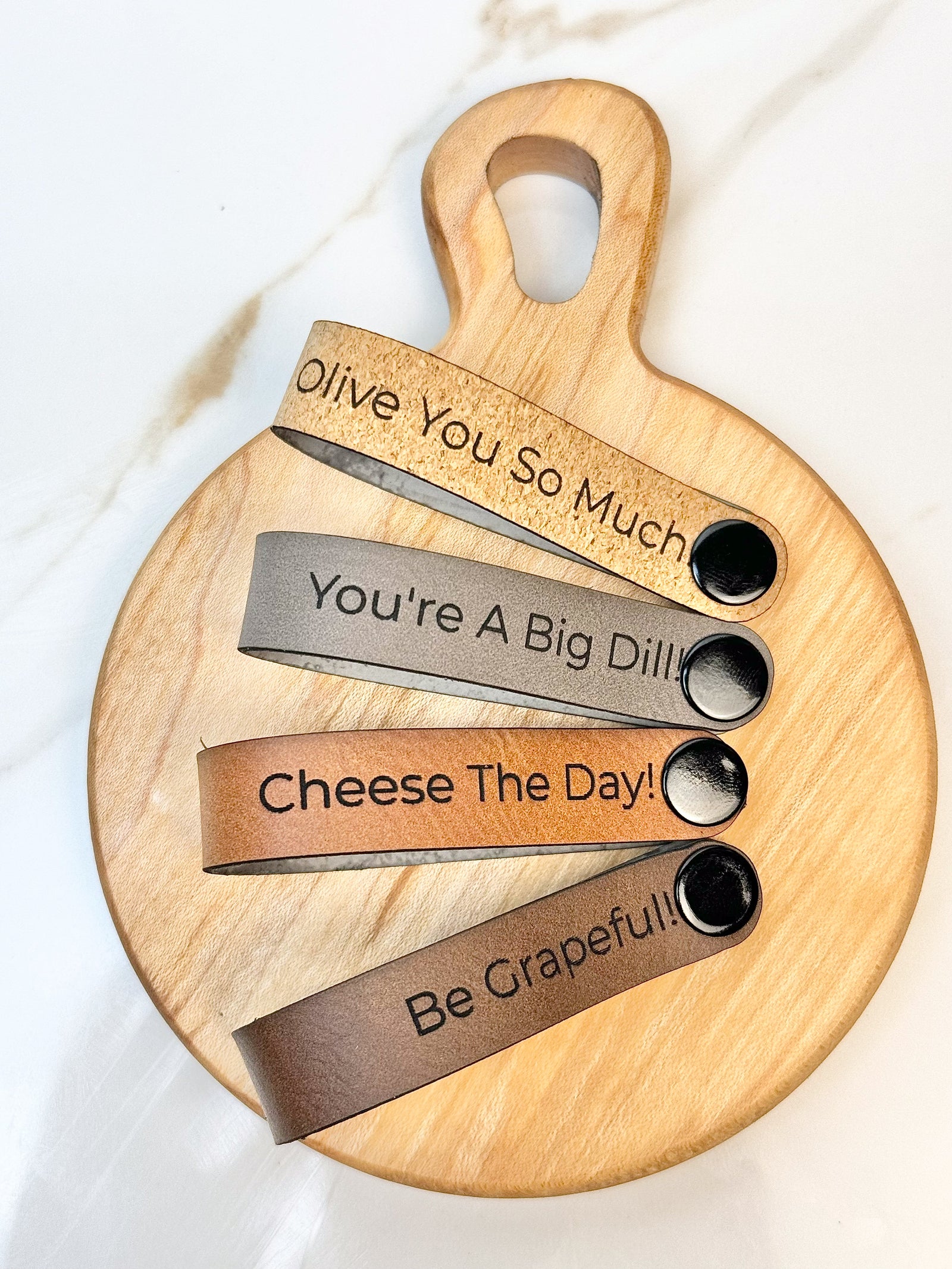 Maple wooden coaster single serve mini charcuterie board set with vegan leather straps engraved with puns: Be Grapeful!!, Olive You So Much, You;re A Big Dill!, and Cheese The Day! Coasters have a natural finish.