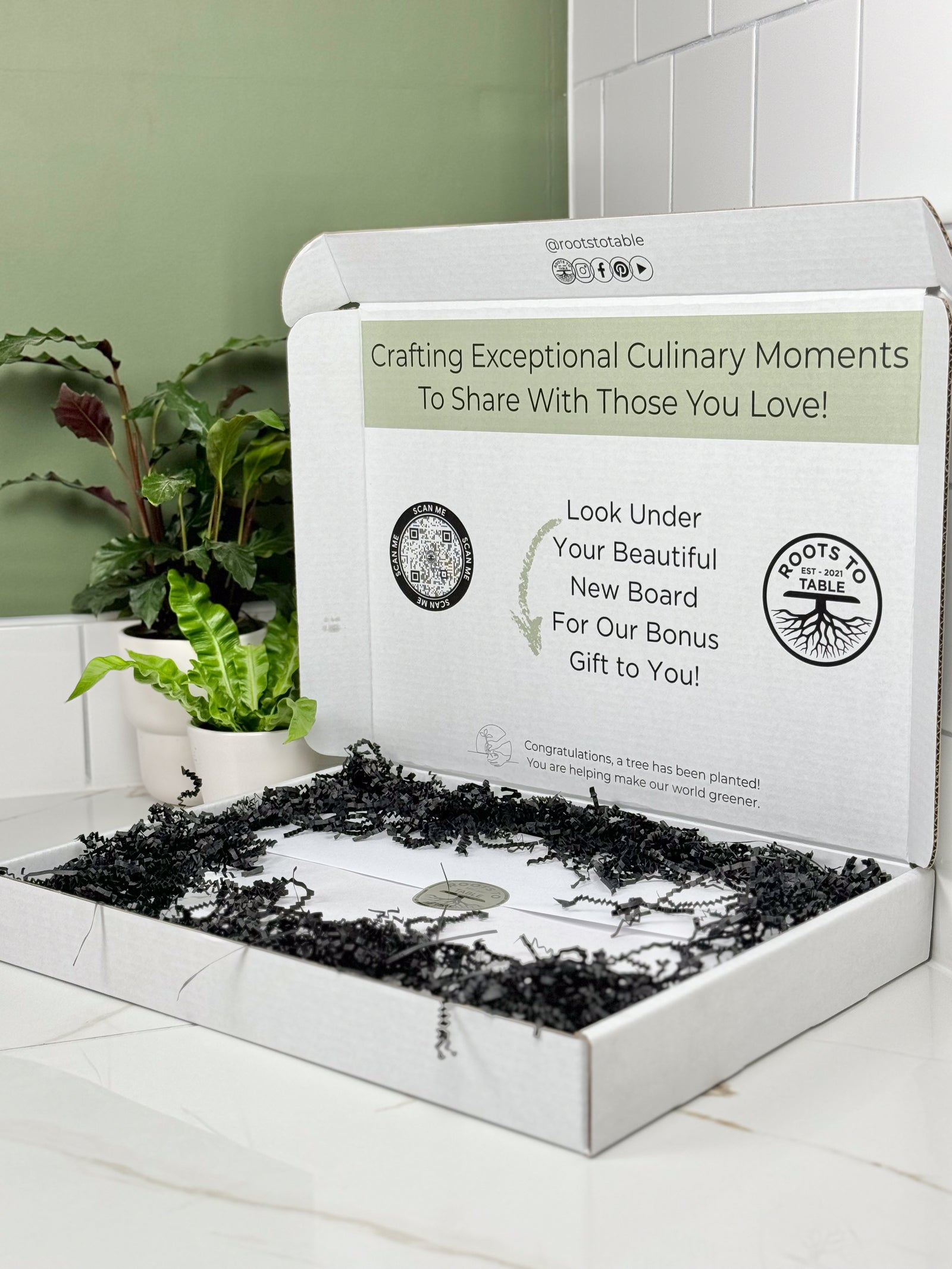 Image depicting the gift box perfectly packaged for gifting wooden walnut and maple cutting and charcuterie boards. The box is white with a scan code and information printed on the inside of the box. The board is wrapped in white paper and black crinkle paper fills the empty space for a finished look.