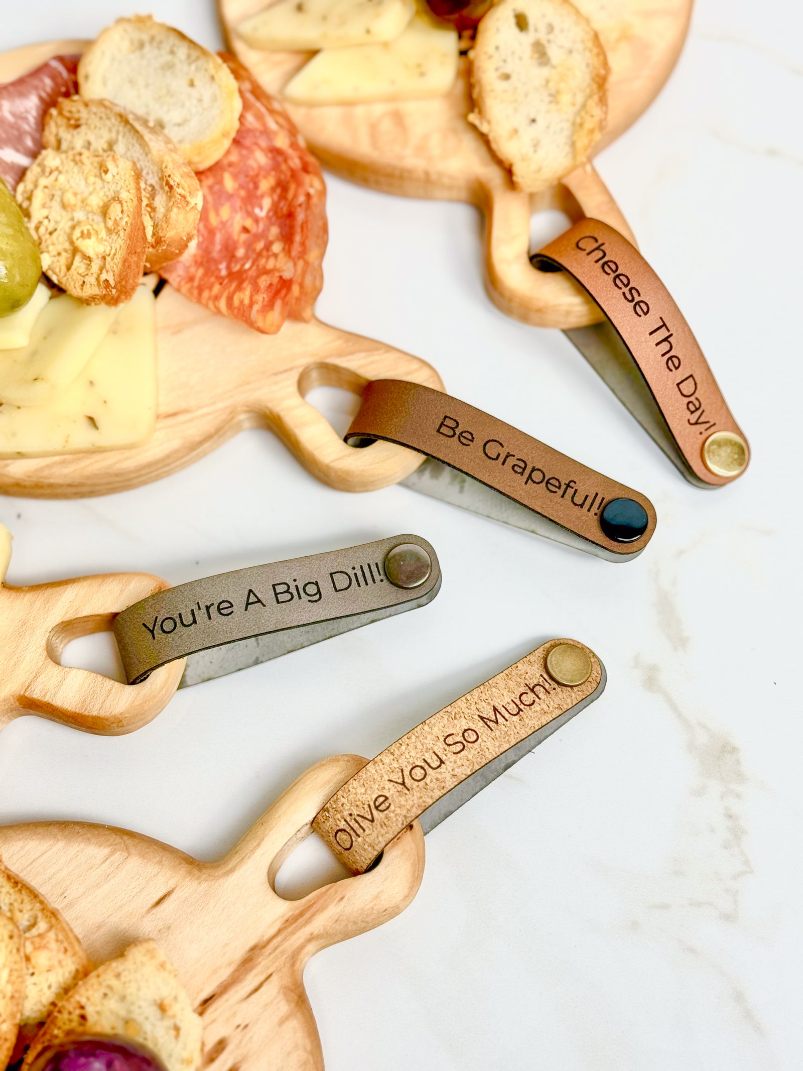 Maple wooden coaster single serve mini charcuterie board set with vegan leather straps engraved with puns: Be Grapeful!!, Olive You So Much, You;re A Big Dill!, and Cheese The Day! Coasters have a natural finish.