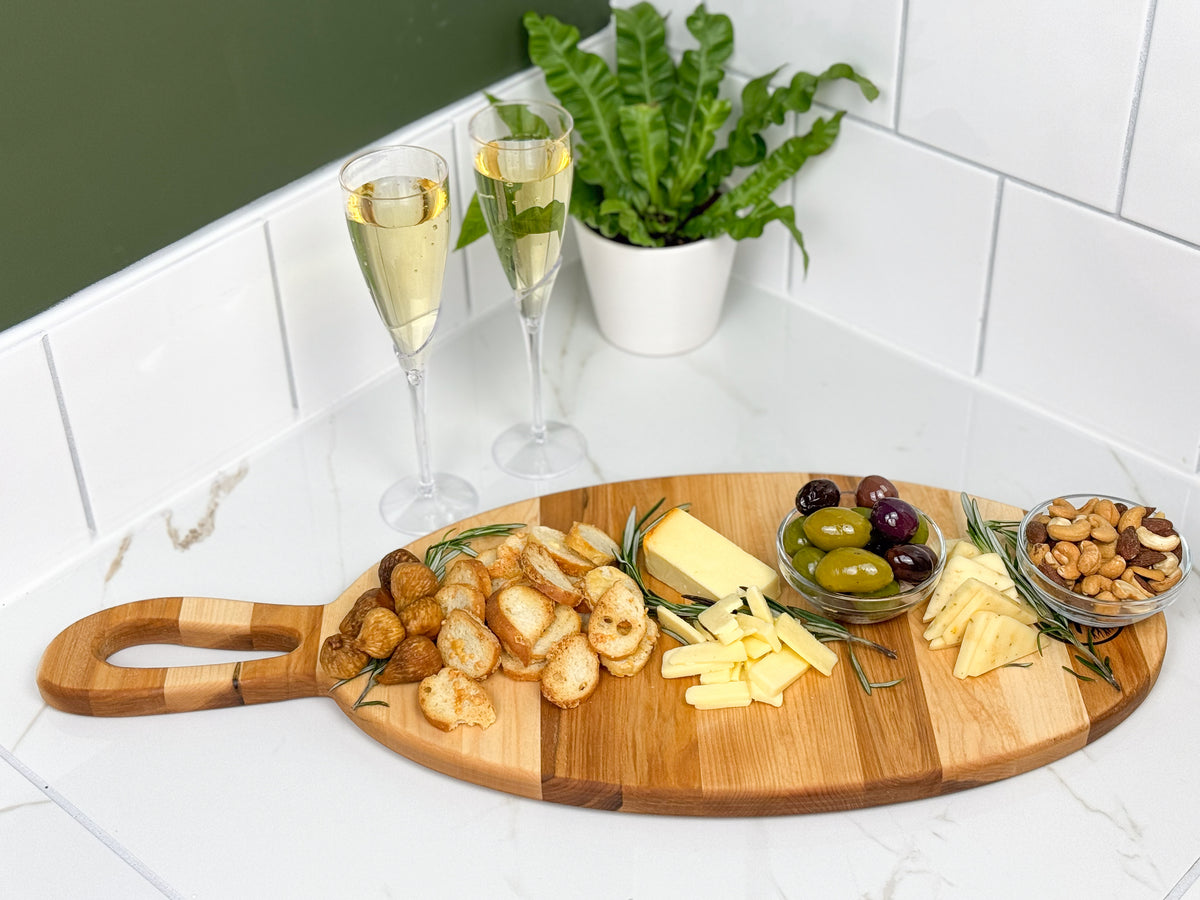 A long oval shaped charcuterie board with handle, with a variety of snacks showcasing the available space.
