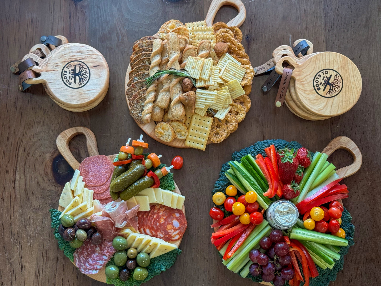 3 round maple charcuterie boards filled completely with a variety of snacks from crackers, to deli meats and cheeses and then a veggie platter. 8 smaller mini round maple charcuterie boards surround the larger three
