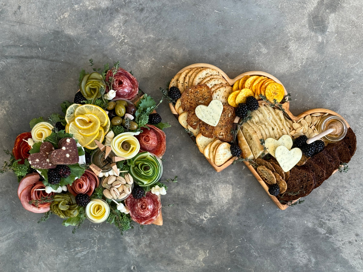 The personalized wooden heart shaped tray is full of crackers, breads, berries and honey. The heart shaped cutting board has a variety of meats, vegetables, cheeses and nuts.