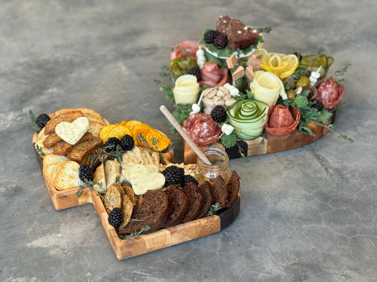 The personalized wooden heart shaped tray is full of crackers, breads, berries and honey. The heart shaped cutting board has a variety of meats, vegetables, cheeses and nuts.