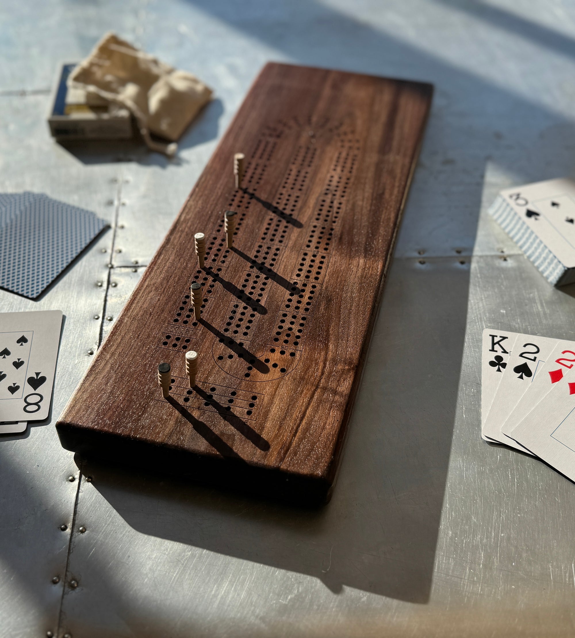 A straight edge walnut wood crib board showcased with pegs and playing cards on a metal table.