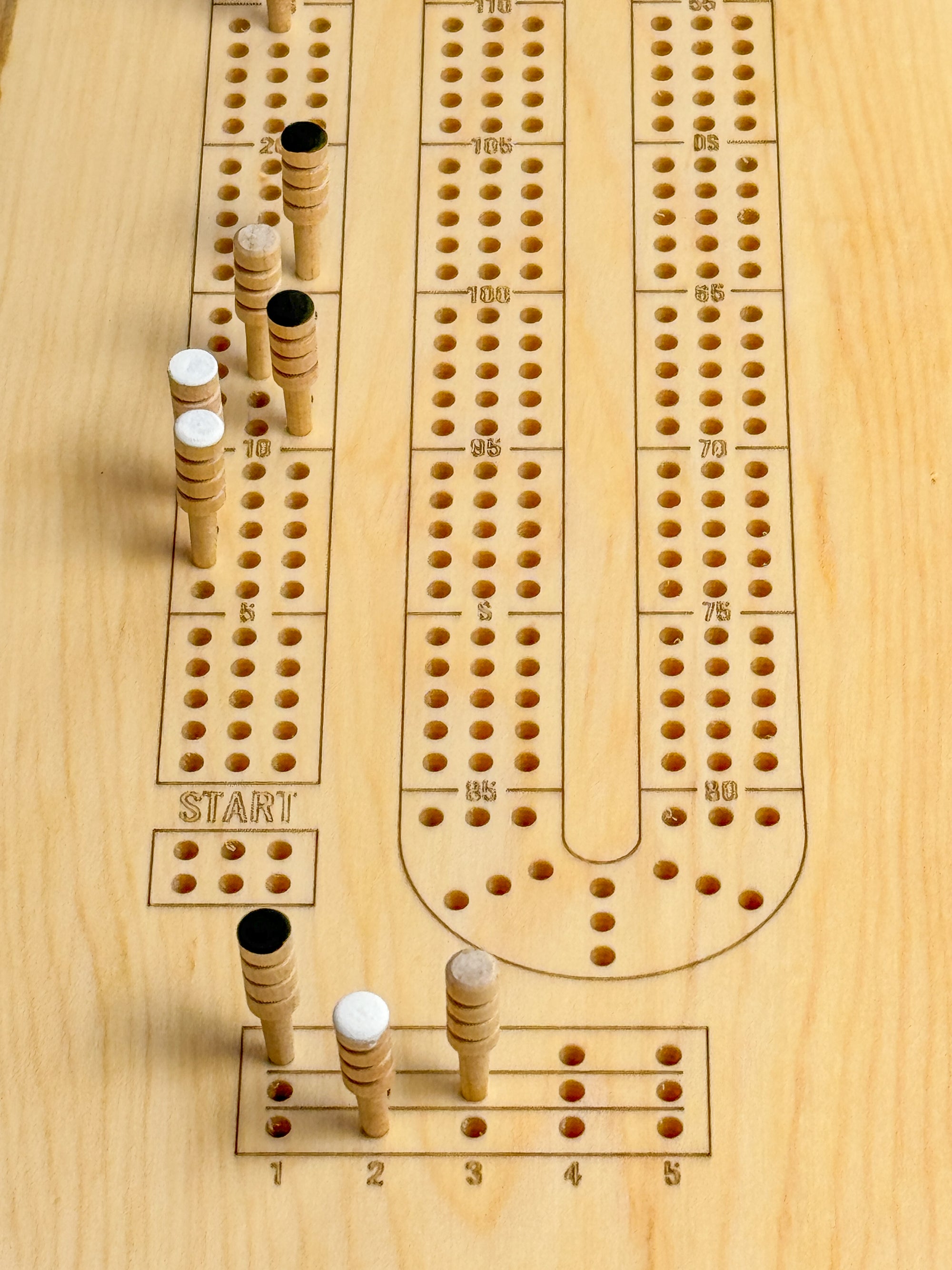 A close up of a maple crib board showing 9 wooden pegs that cab be purchased as as a set