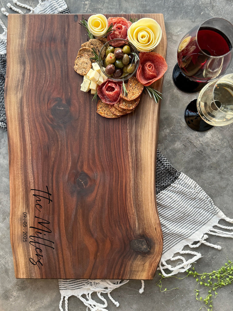 Black Walnut Live Edge Rustic No handle 26x 13 Cheese Board and cutting board with a beautiful arrangement of meats, cheeses, fruits and other foods with a large personalized engraving.