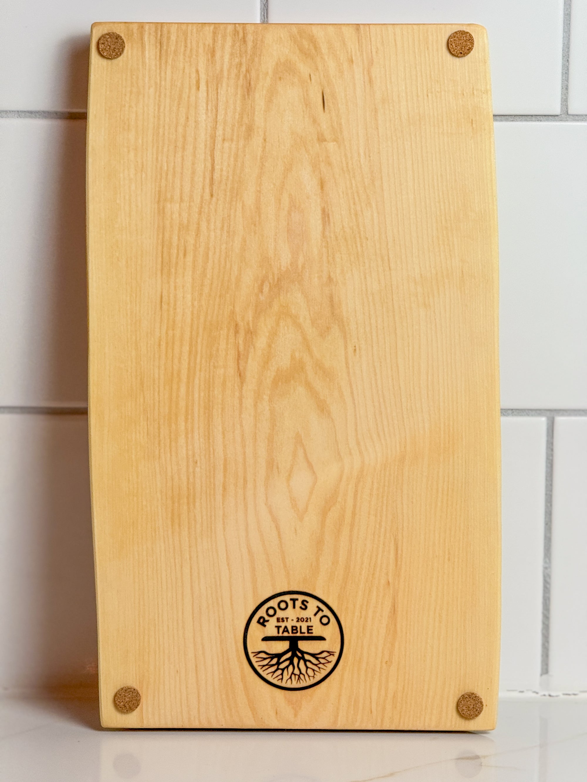 This image shows the back of a maple love edge crib board with the company logo stamped at the bottom of the board. 4 small cork/ felt  plastic stick on feet are adhered to each corner.