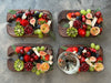 Four wooden black walnut wine and appetizer trays, beautifully arranged with fresh fruits, including strawberries, grapes, figs, cherries, and kiwi, with one tray featuring a wine glass in its designated holder