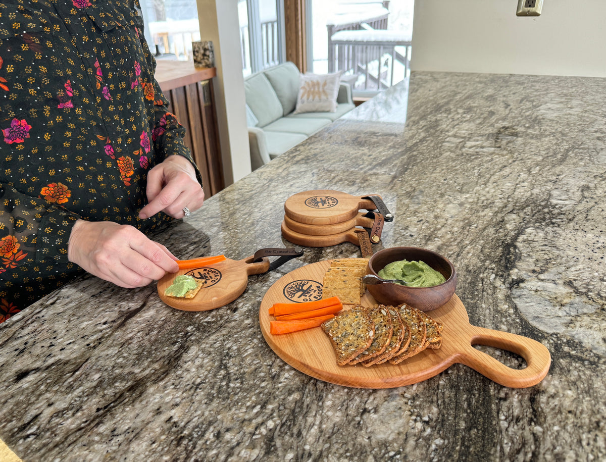 This image displays a person using a small individual round maple charcuterie boards that is being filled from a larger round maple board that goes with the set of 5