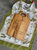 A handwritten brownie recipe is engraved onto a maple cutting board, displayed on a  vintage tea towel.