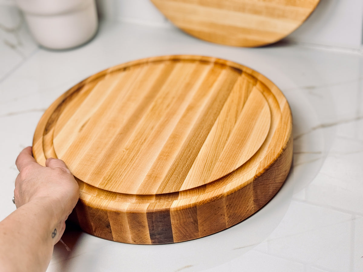 A hand holds a two inch round maple cutting board to showcase the circumference and thickness of the board demonstrating the sturdiness and quality.
