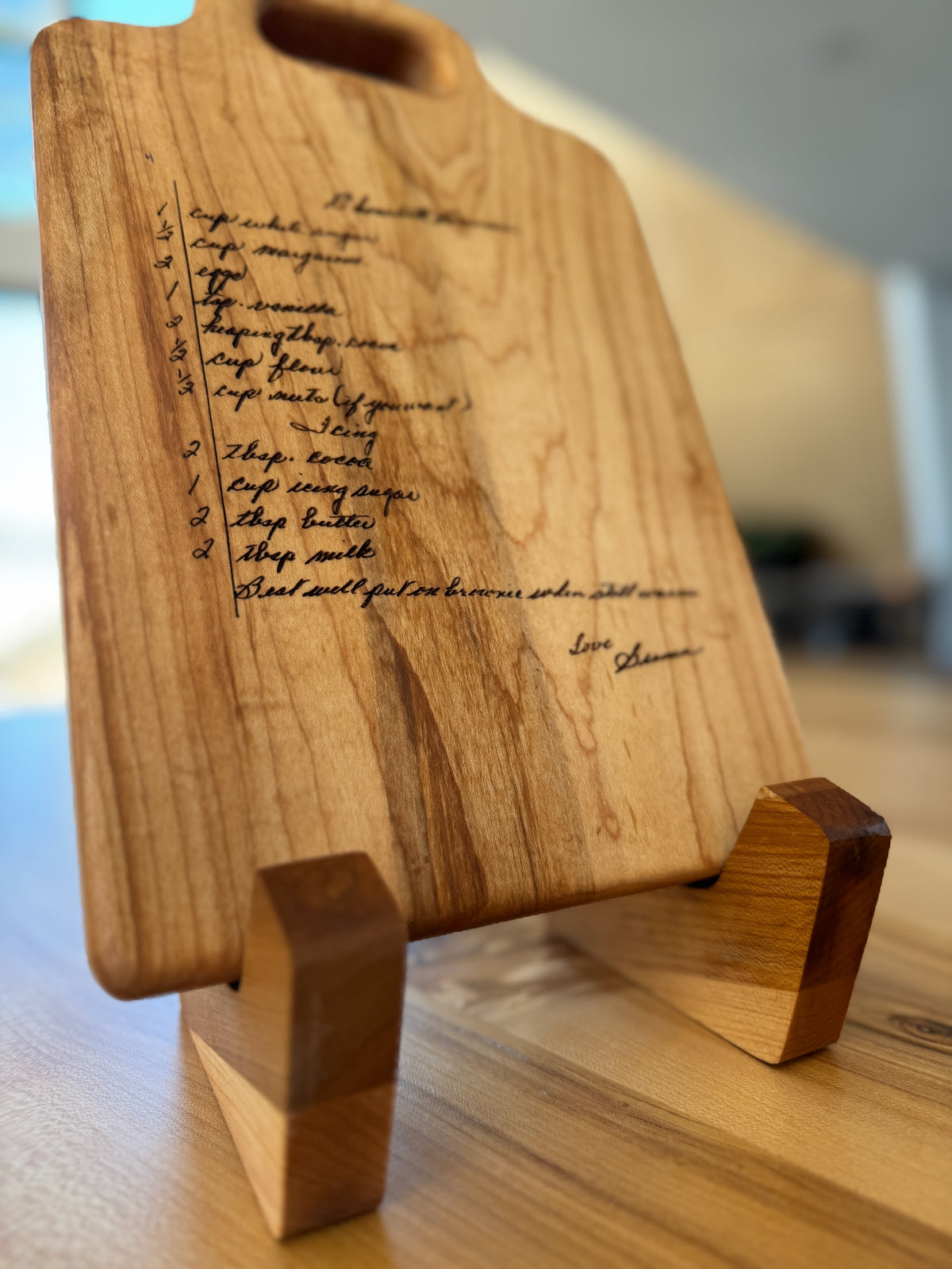 Maple cutting board with engraved hand written brownie recipe resting on a two piece maple board stand