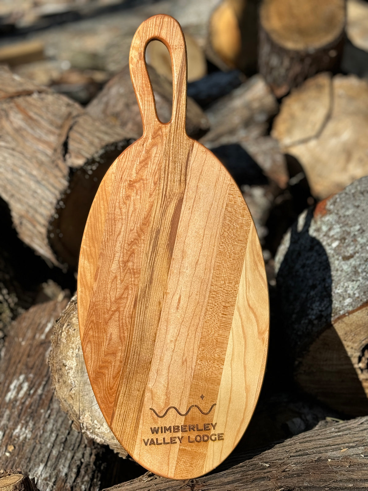A long oval shaped charcuterie board with handle, almost looks like a fish board features a company logo engraving