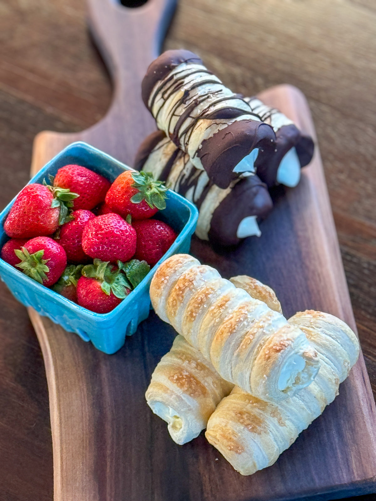 Cannoli and basket of strawberries served on a live edge walnut charcuterie board.