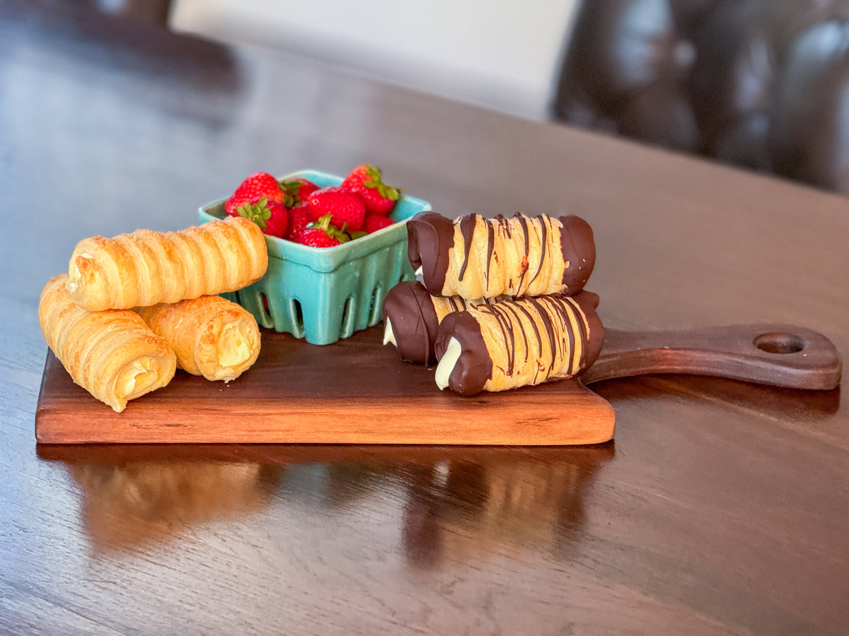 Side view of Cannoli and basket of strawberries served on a live edge walnut charcuterie board.