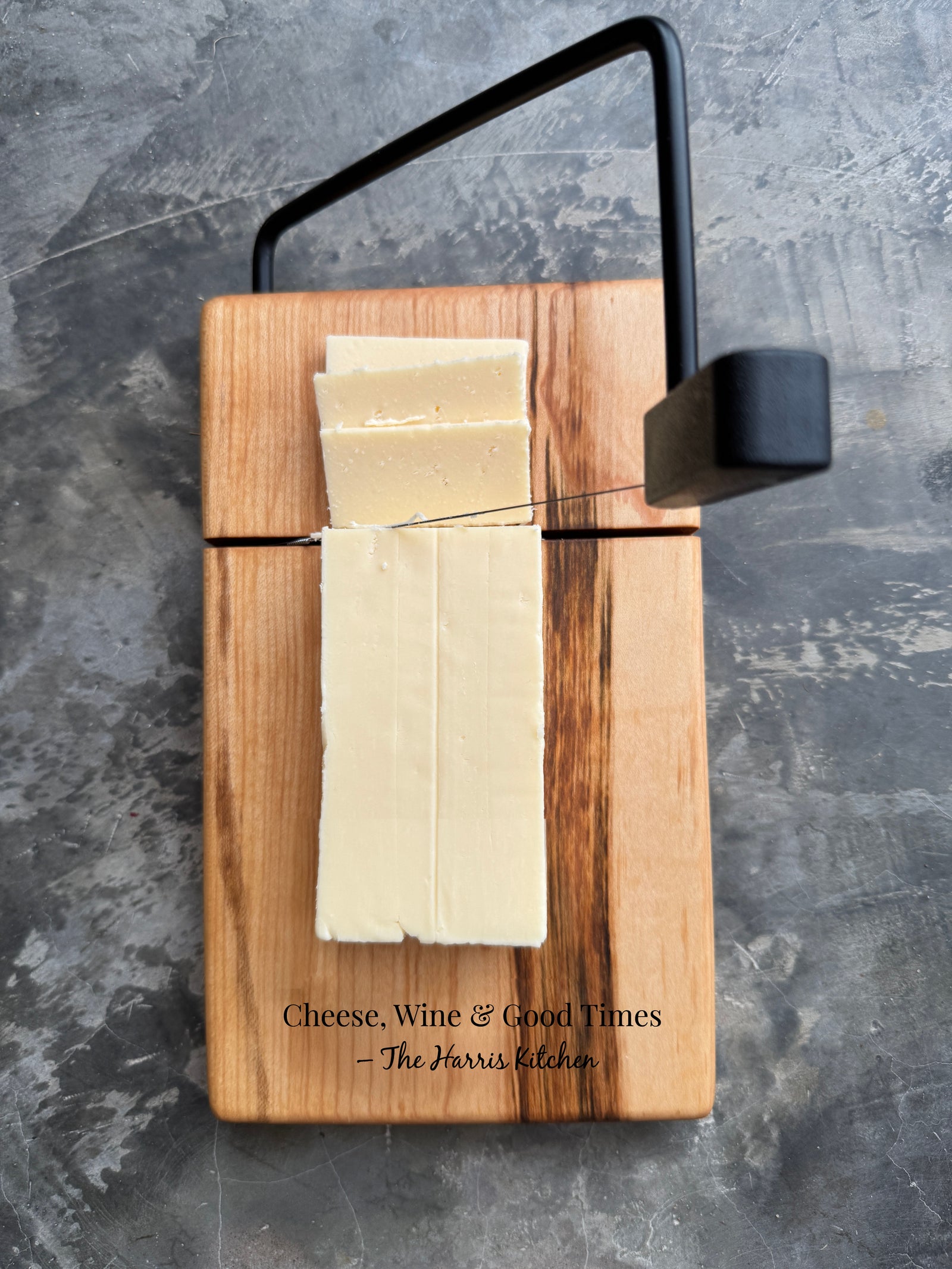 2 cheese slicer cutting boards on a countertop side by side. One cheese slicer has a wlanut base, and the other has a maple wood base. both cheese wire slicer boards are engraved with a fun quote. The board measures 5.75 x 9.5 x 1 inch thick, with wire slicer attachment. Custom Engraving available