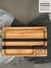 A handcrafted cutting board made from alternating strips of maple and walnut wood, featuring a juice groove for functionality and a smooth, polished finish. A customized letter W engraving surrounded by laurel leaves in the corner.