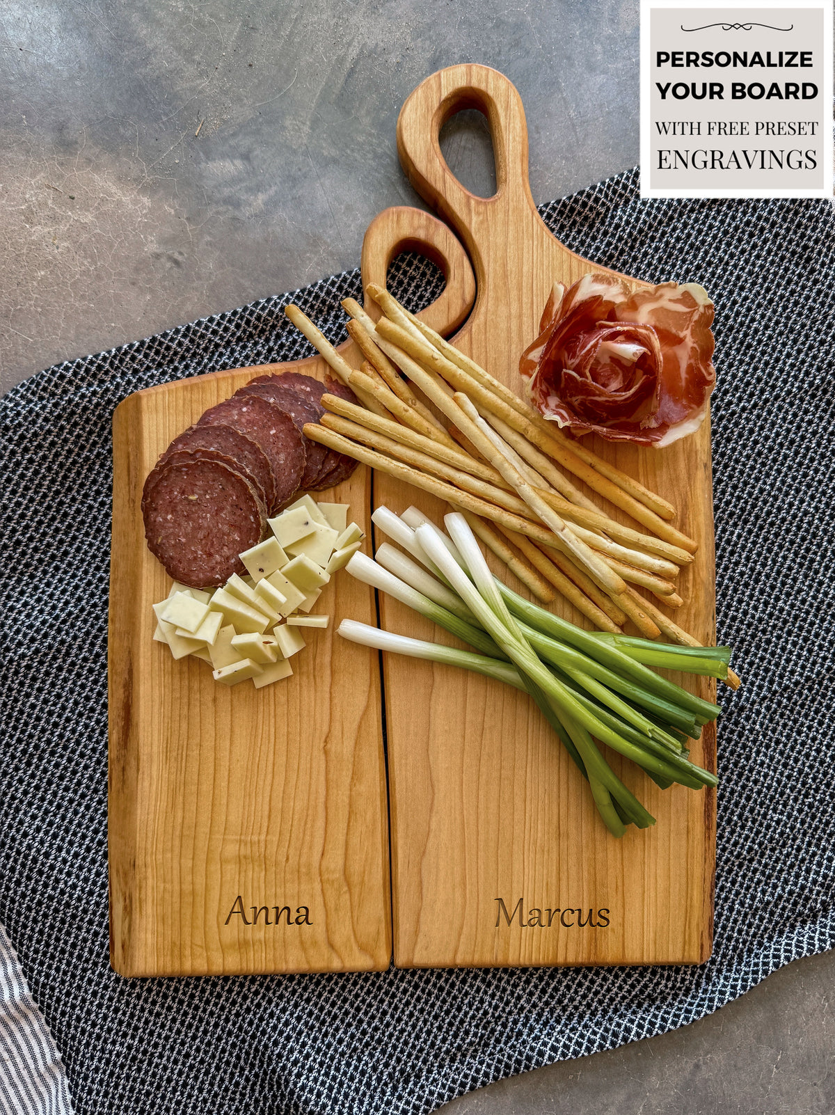 Two personalized wooden Live Edge charcuterie boards engraved with Anna and Marcus, nestle into each other creating one seamless board. The handles snug into one another like a friend resting resting their head on another's shoulders.